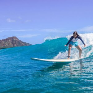 girl standing on surfboard riding wave with diamond head in background